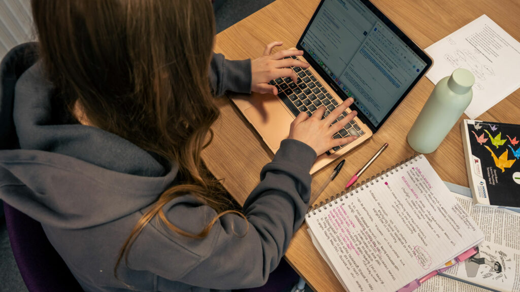 A student sat at a desk working on a laptop