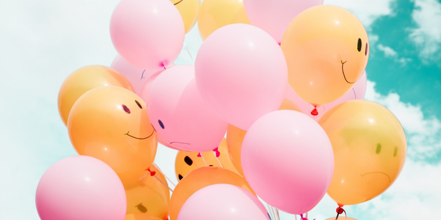 bunch of pink and orange balloons with sad and happy face designs