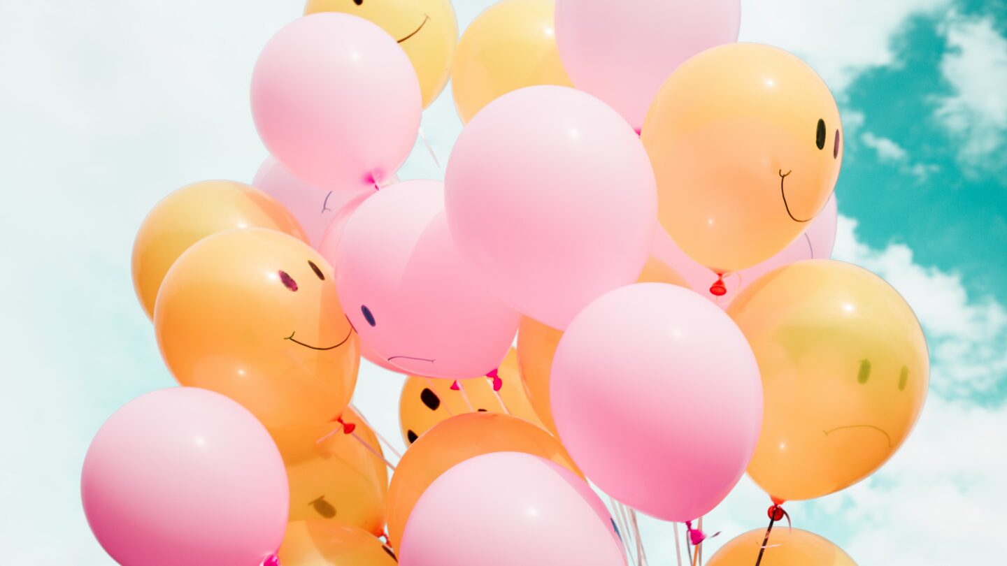 bunch of pink and orange balloons with sad and happy face designs