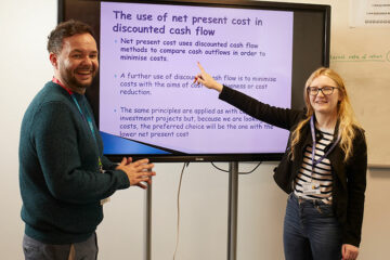 A student and lecturer stood at a TV screen with information showing