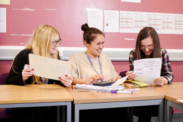 Three students sat at a table looking at paperwork