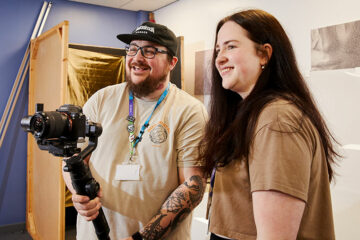 A student and a lecturer looking at a camera
