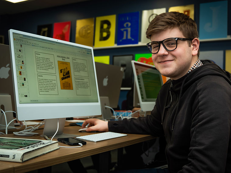 A graphic design student sat in front of an Apple Mac