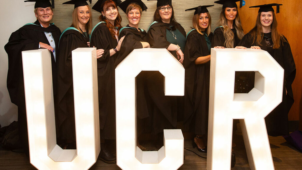 A group of graduates stood by the large UCR letters