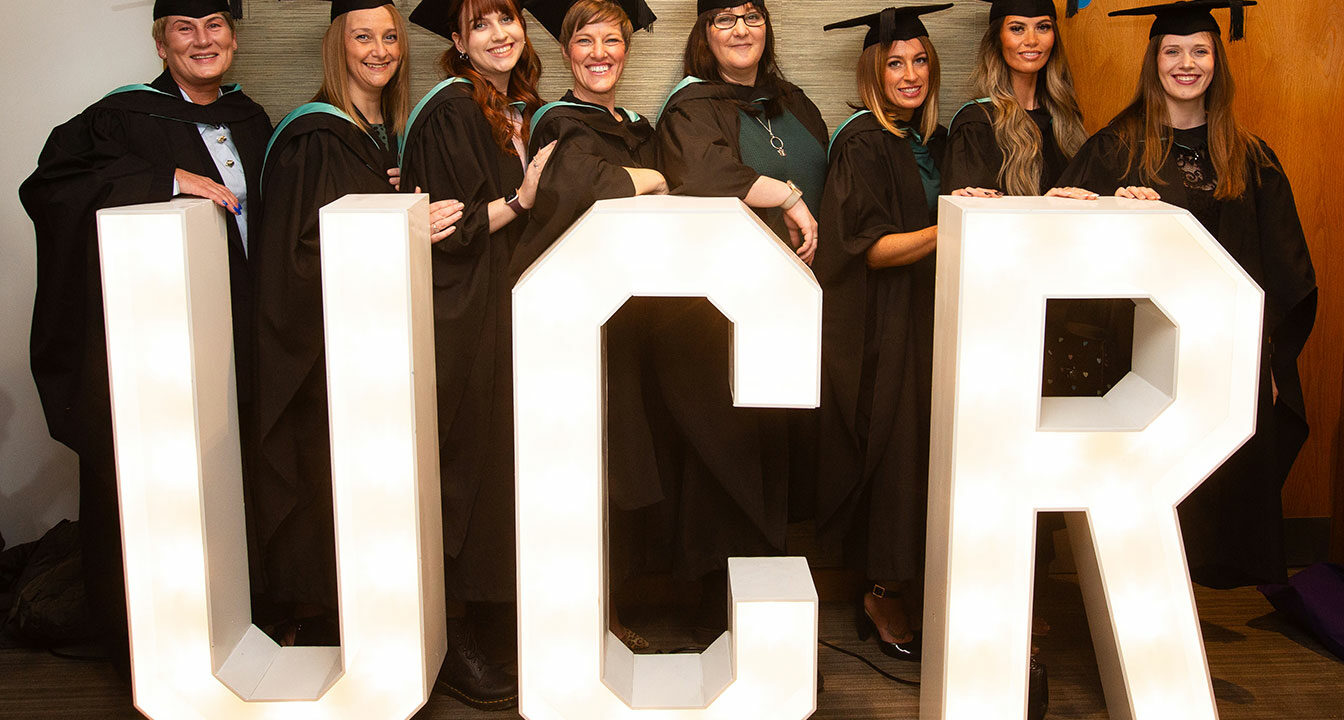 A group of graduates stood by the large UCR letters