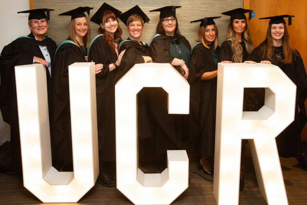 A group of graduates stood by the large UCR letters