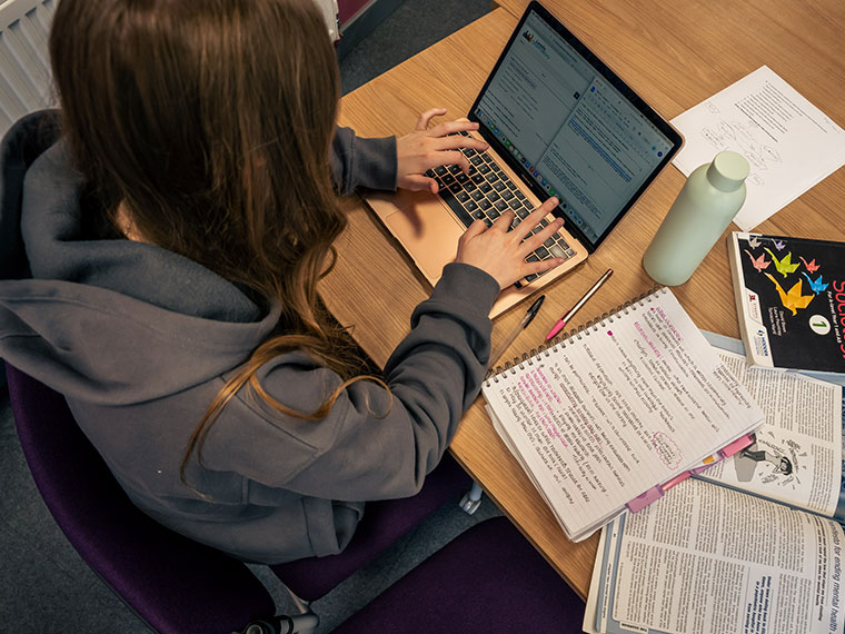 A student sat at a desk working at a laptop