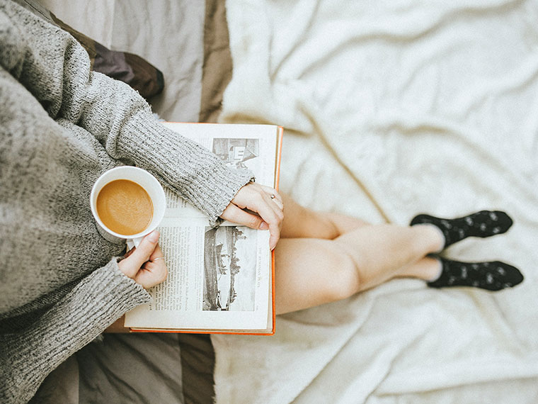 Someone sat relaxing with a cup of tea looking at a book