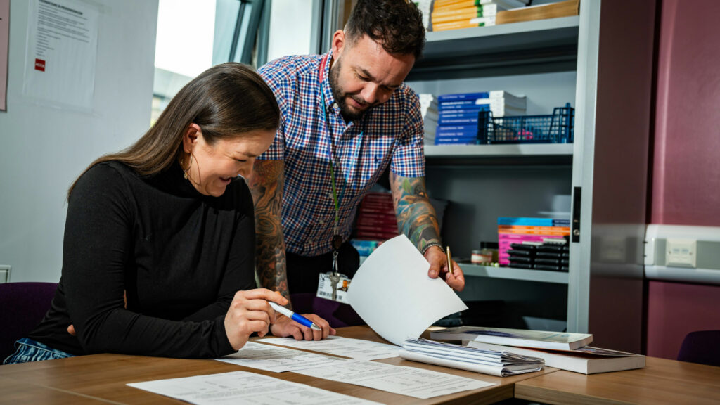 An adult learner working at a desk recieving advise from the tutor