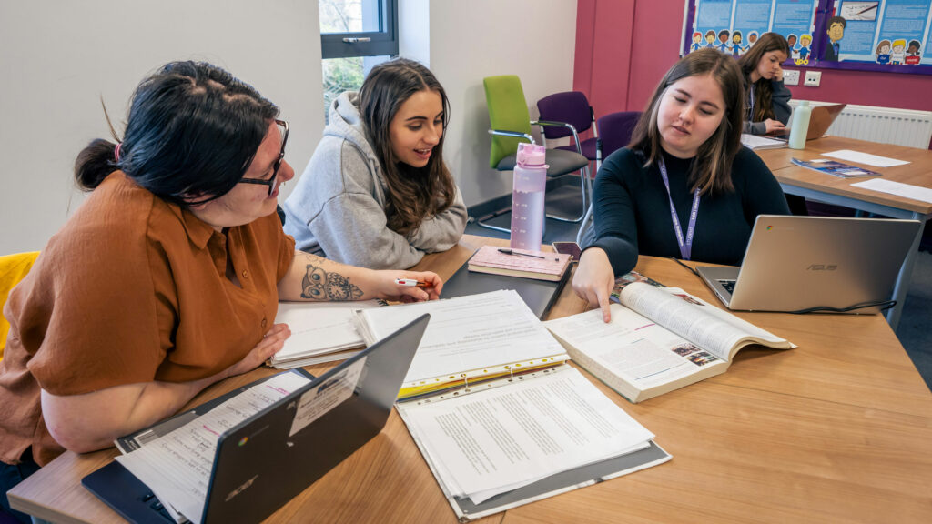 Three students sat around a desk doing their work