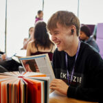 A smiling student sat at a table in a social space at University Centre Rotherham