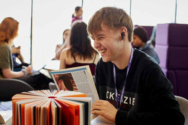 A smiling student sat at a table in a social space at University Centre Rotherham