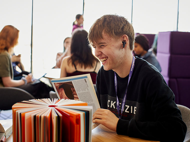 A smiling student sat at a table in a social space at University Centre Rotherham
