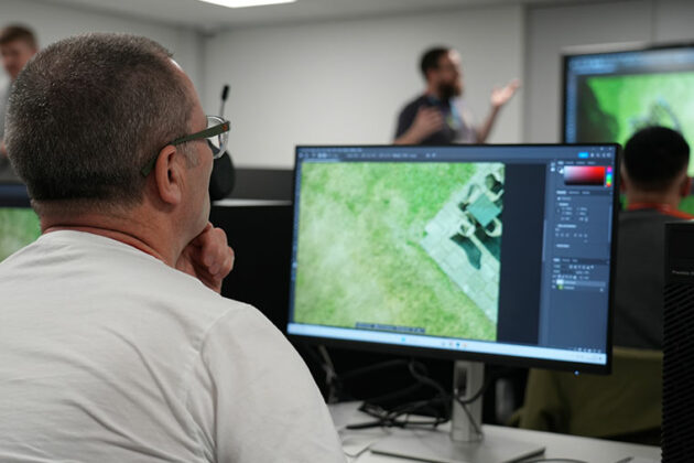 An adult sat in front of a computer with the lecturer in the background