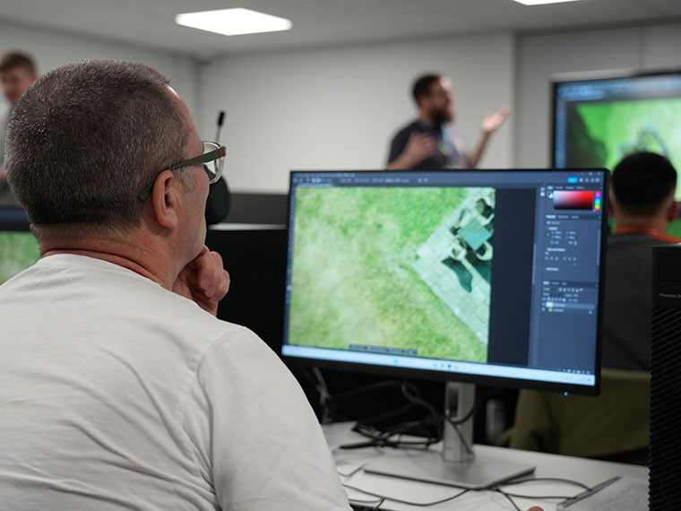 An adult sat in front of a computer with the lecturer in the background