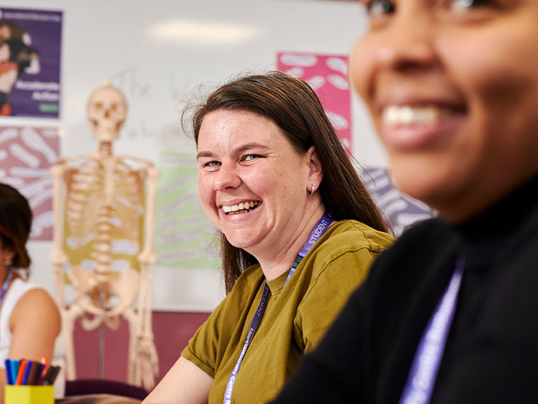 Two smiling health students with a skeleton in the background