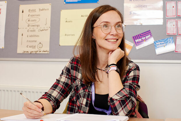 A smiling student sat at a table with a pen in their hand ready to write