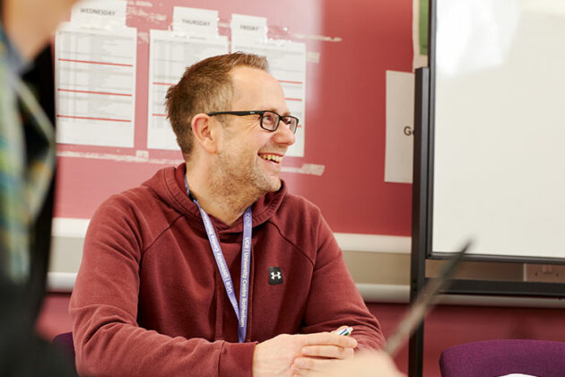 Someone sat at a desk smiling whilst looking away from the camera