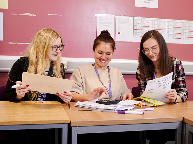 Three adult learners sat at a table looking at doucments together
