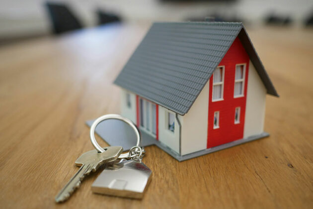 A small model of a house on a table with a key laid to the side of it