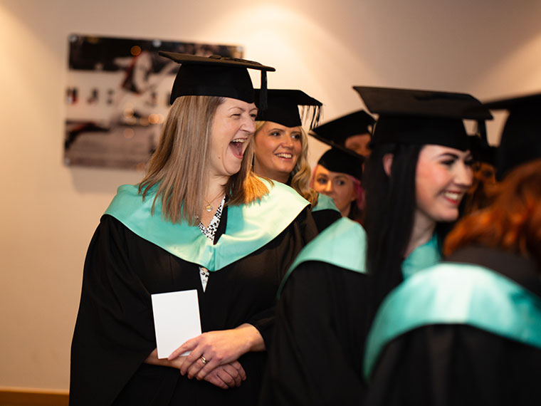 Graduands lining up ready to enter the ceremony room, one person with a big smile