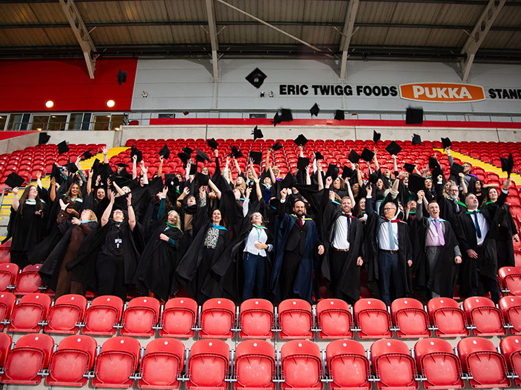 A large group of graduates throwing their hats up in the air in the stands at Rotherham United FC ground