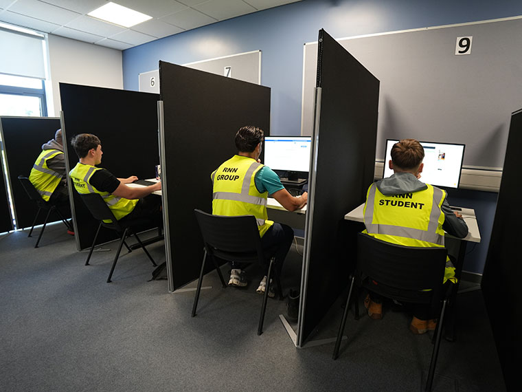 Four people sat in separate cubicles at computers