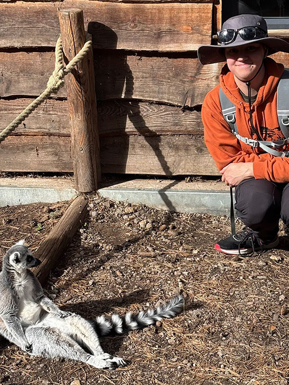 UCR Animal Management student Finn smiling crouched next to an animal