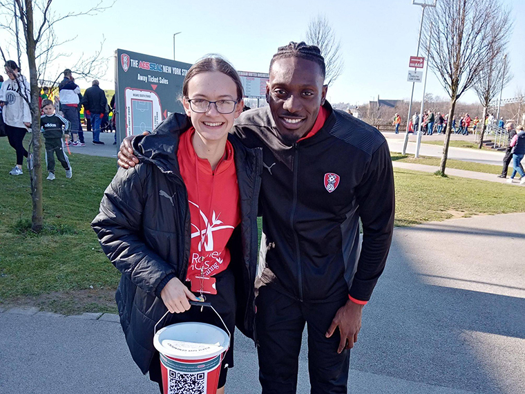 Hannah smiling stood with a male whilst holding a collection bucket