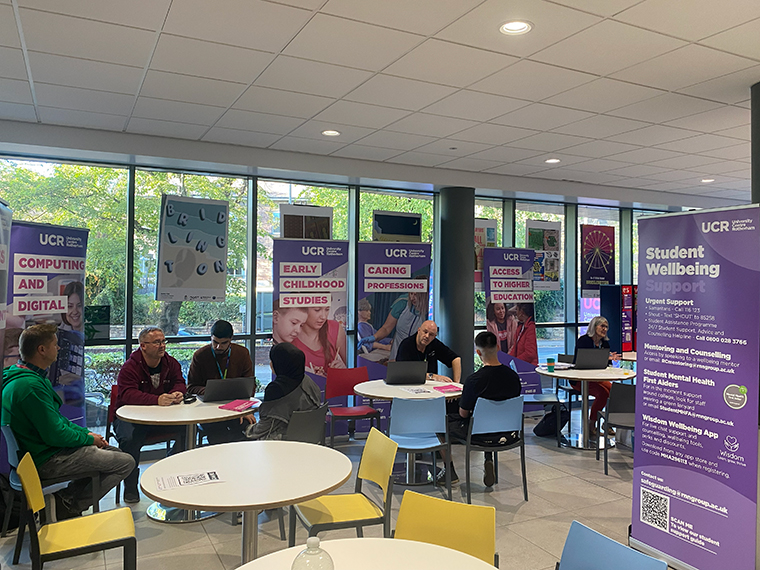 People sat around three small round tables, pull up banners behind them for different course areas
